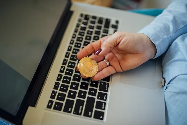 Hand holding a gold bitcoin token over a laptop keyboard