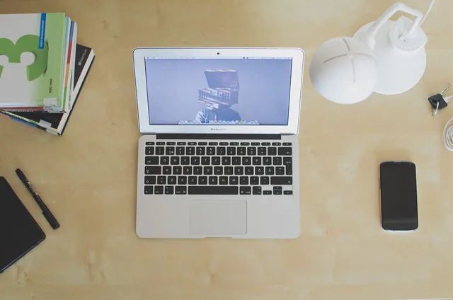 MacBook on a desk seen from above, next to a phone and notebooks